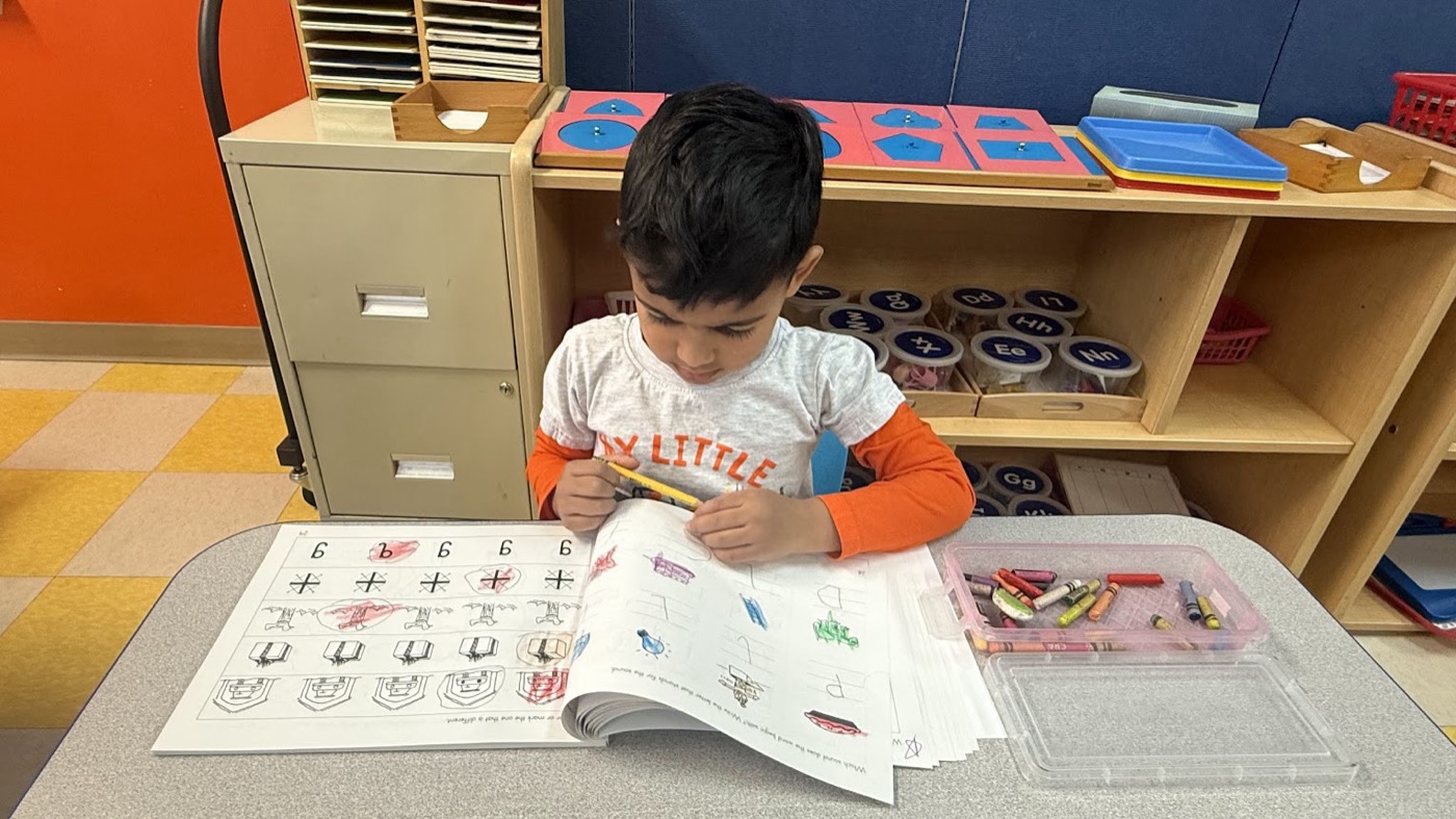 Child practicing writing and coloring at a classroom table